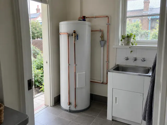 Hot water cylinder with copper pipework in a tiled laundry beside a sink in Clovelly